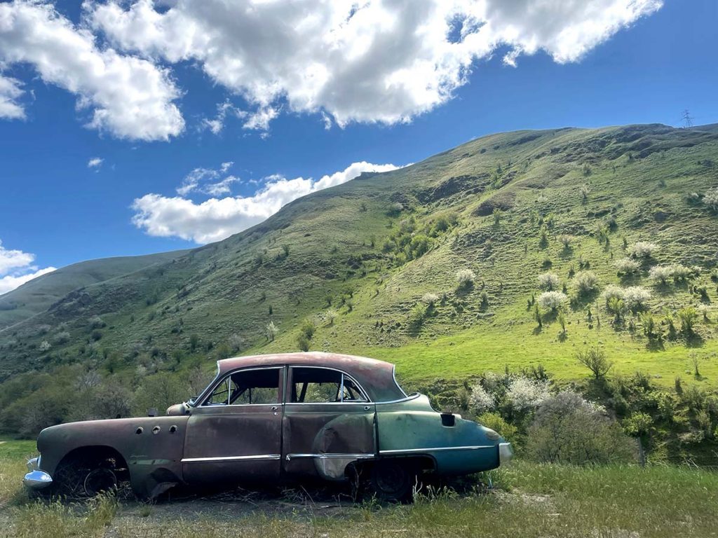 Old Broken Car in front of green hills