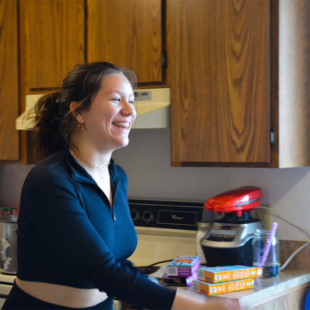 A woman in a black shirt moves across the room, a big smile on her face.